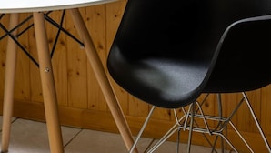 Un interior de madera con una mesa redonda, una silla negra, un cuenco de fruta, una taza de café y una ventana con vistas a árboles.