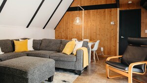 Una sala de estar moderna con un sofá modular, un sillón de cuero negro y un comedor con una mesa y sillas blancas.