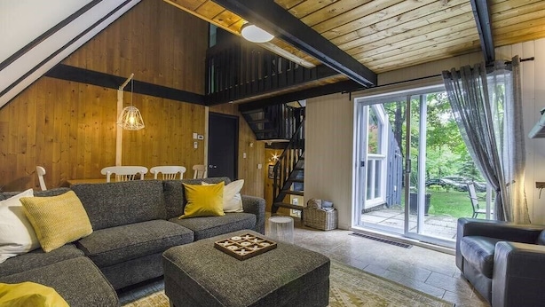 Una sala de estar moderna con un sofá gris, un reposapiés y una escalera que conduce a un nivel superior.