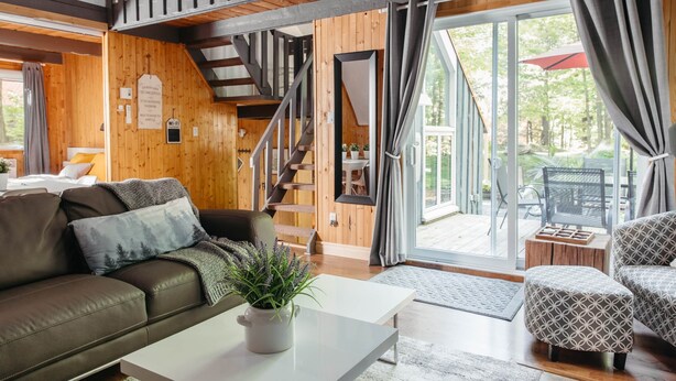 Un interno moderno con una scala in legno, un divano, un tavolino da caffè e vista sull'esterno.