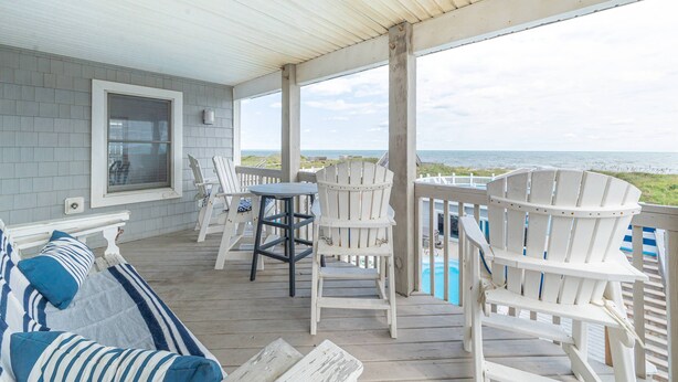 Eine überdachte Veranda mit weißen Adirondack-Stühlen, einem Tisch und einer Bank mit gestreiften Kissen.