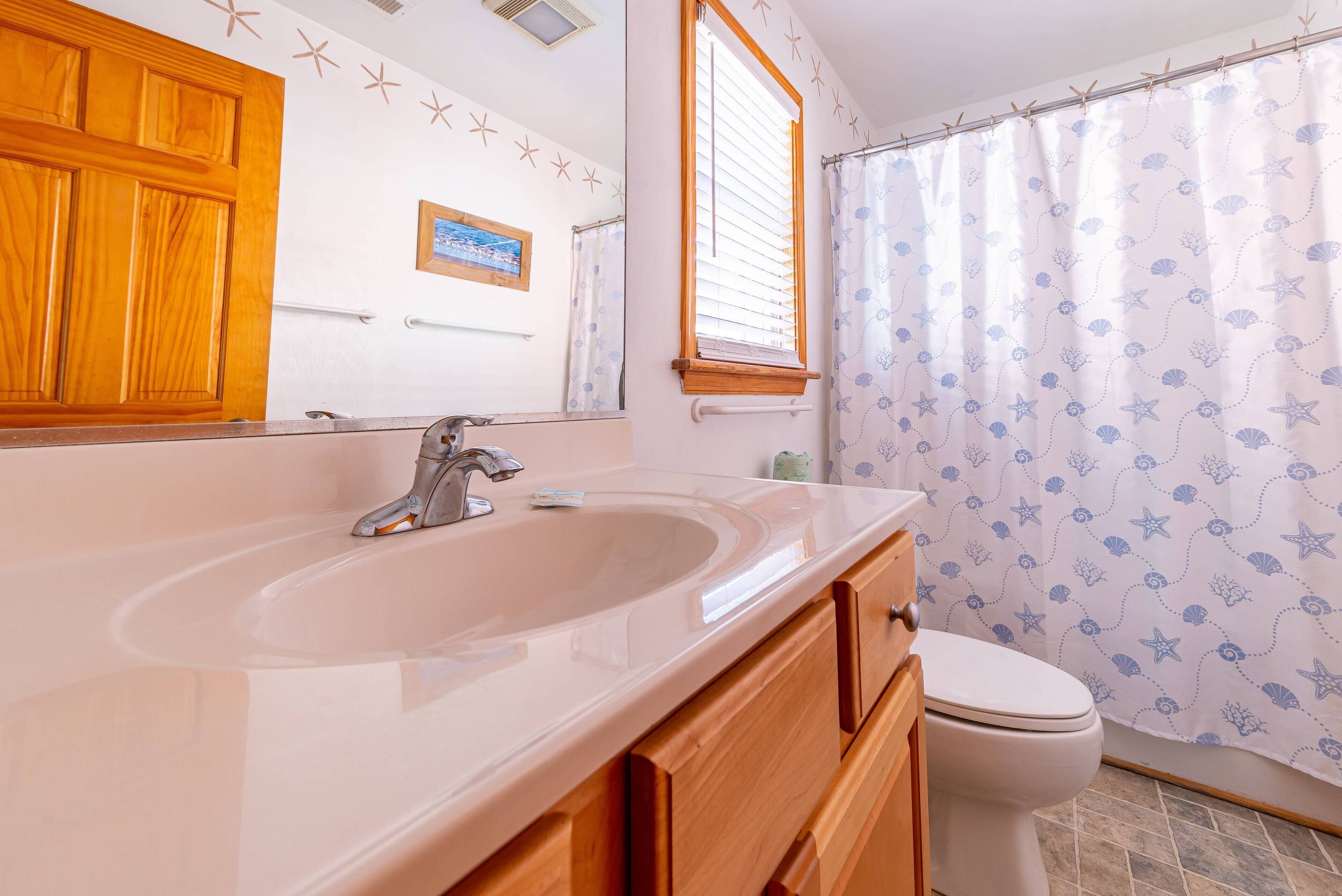 Une salle de bain avec un meuble-lavabo en bois, un évier, un miroir, des toilettes et un rideau de douche orné d’un motif d’étoile de mer.