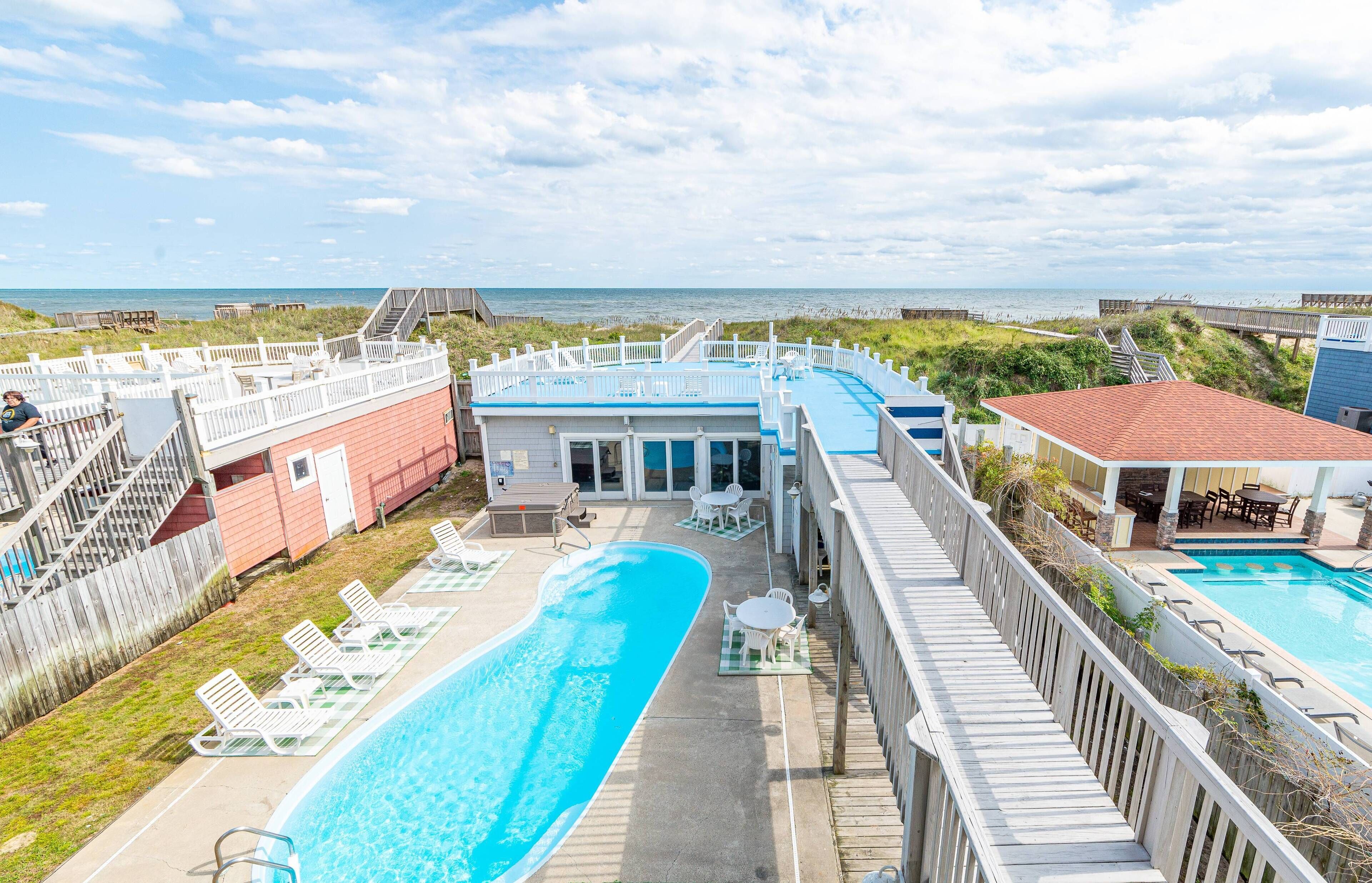 Ein Poolbereich mit Blick auf den Strand, eine Holzterrasse und ein Gebäude mit blauem Dach.