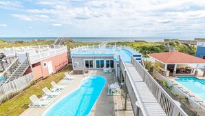 Ein Poolbereich mit Blick auf den Strand, eine Holzterrasse und ein Gebäude mit blauem Dach.