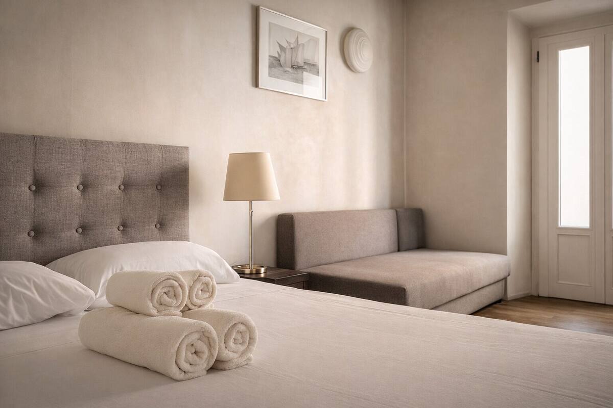 A hotel room with a large bed, a sofa, a bedside table with a lamp, and a framed picture on the wall.