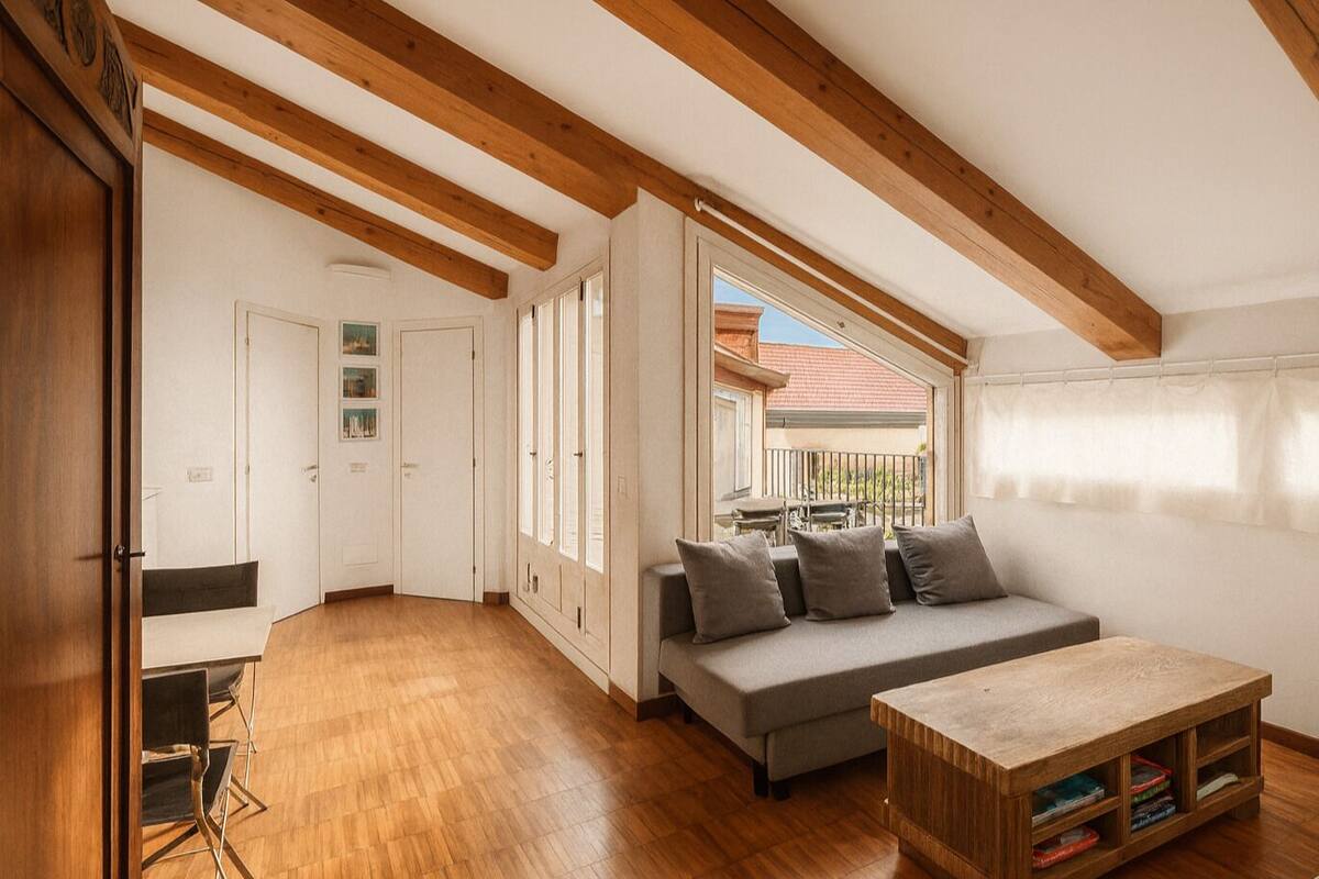 A spacious room with wooden beams, a sofa, a small table, and a balcony with a view.