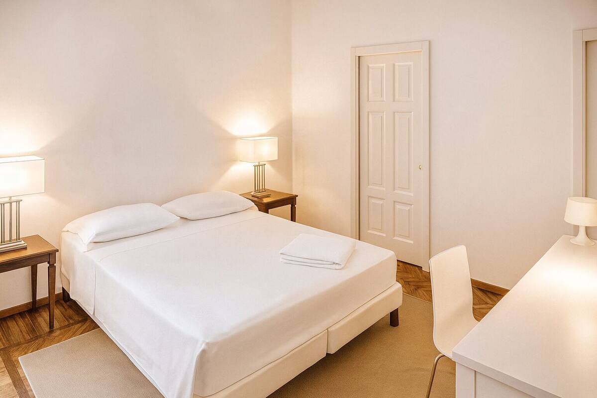 A neatly arranged hotel room with a bed, bedside tables, a desk, and a door.