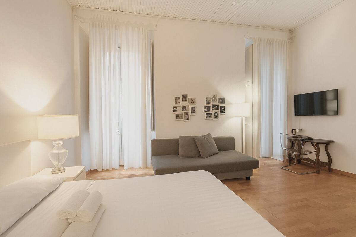 A hotel room with a bed, a sofa, a TV, and a table with a lamp.