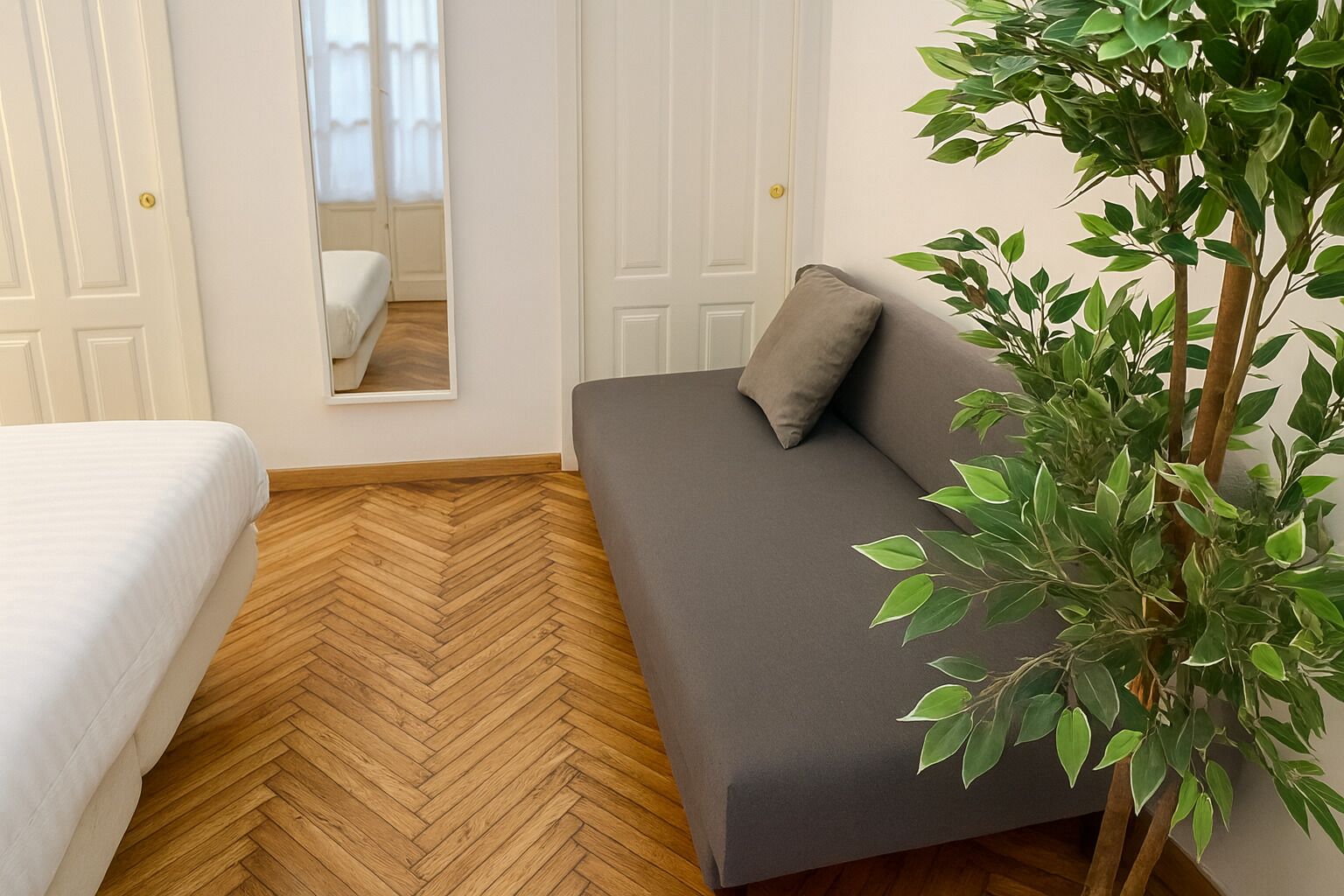 A room with a bed, a sofa, a mirror, and a potted plant.