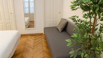 A room with a bed, a sofa, a mirror, and a potted plant.