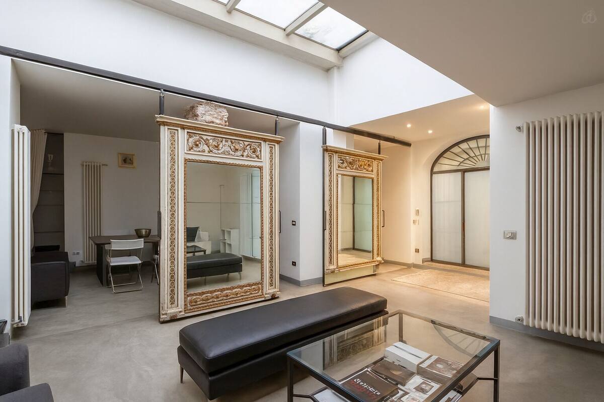 A spacious living area with a large mirror, a bench, and a glass coffee table.