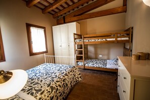A bedroom with a bunk bed, a white wardrobe, a window with curtains, and a brick floor.