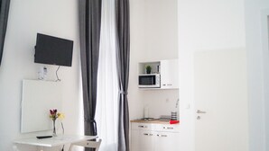Habitació petita i moderna amb escriptori, televisió de pantalla plana, microones i armariet.