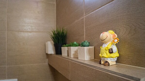 Een badkamer met een plank waarop een zacht knuffeldiertje, een potplant en een klein decoratief object staan.