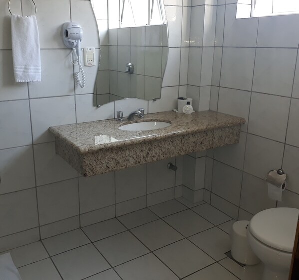 A bathroom with a granite countertop sink, a mirror, a hairdryer, and a toilet. - Verde Vale Hotel (Videira)