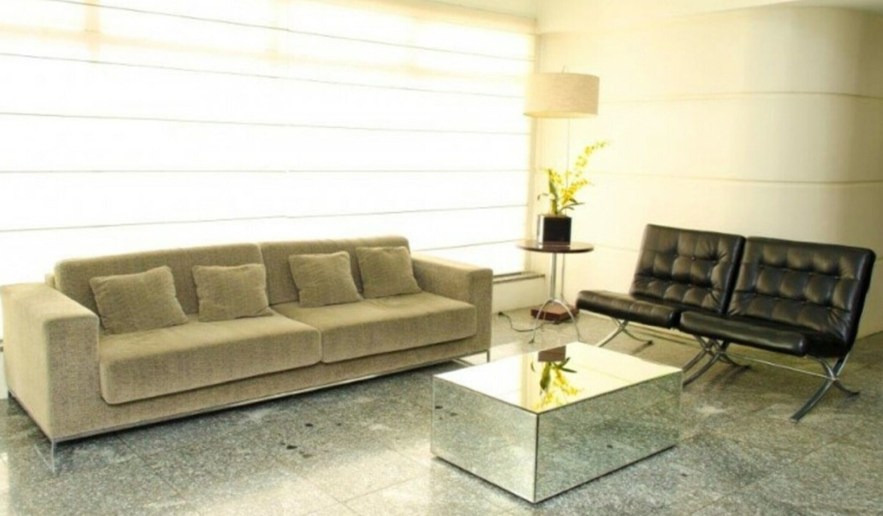 Uma sala de estar moderna com um sofá bege, um sofá de couro preto e uma mesa de centro de vidro.