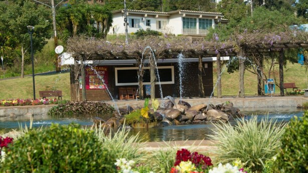 Un jardin avec un bassin, une pergola ornée de fleurs et un bâtiment en arrière-plan.