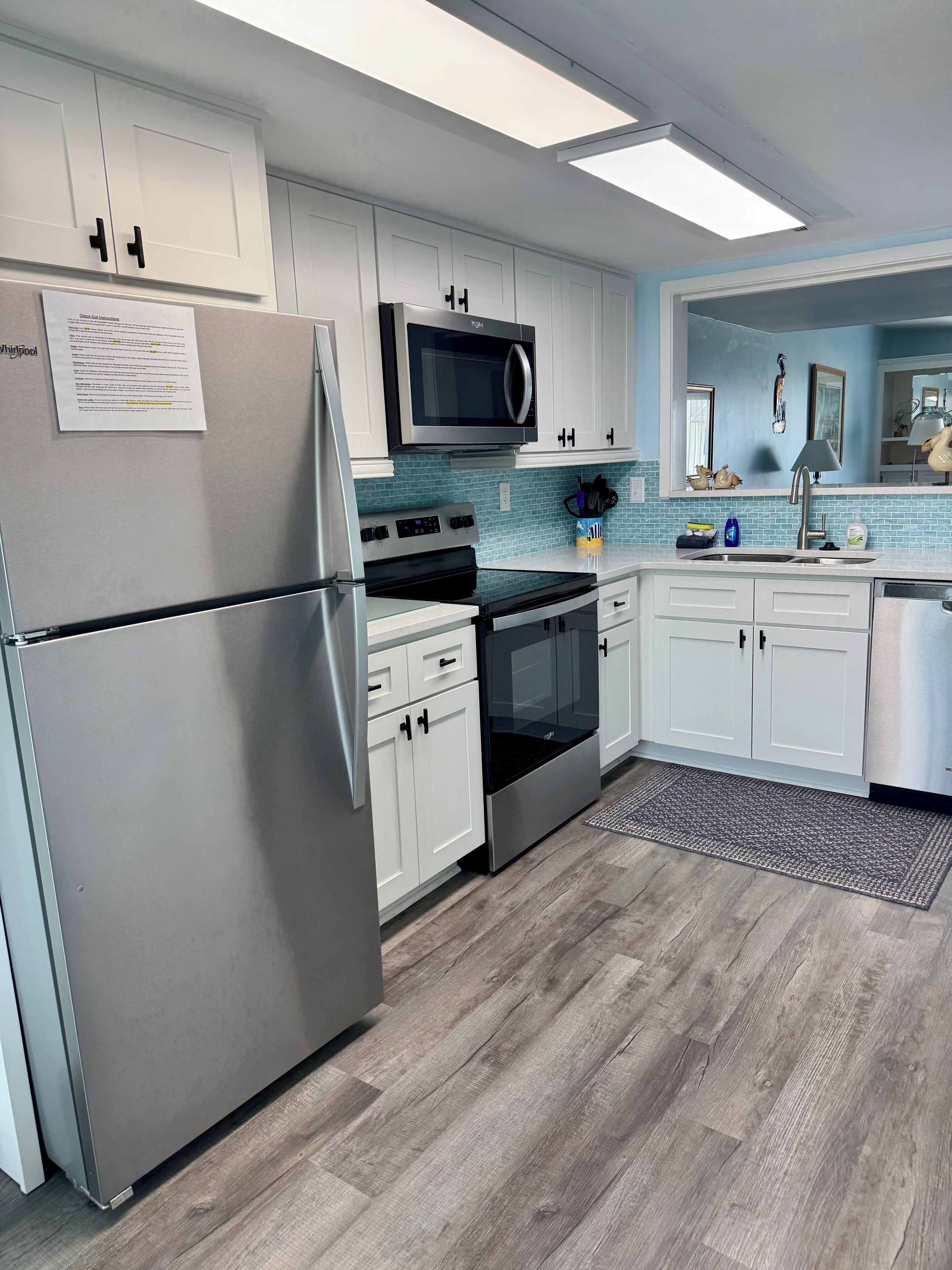 A modern kitchen with white cabinets, a stainless steel refrigerator, a microwave, an oven, and a dishwasher.