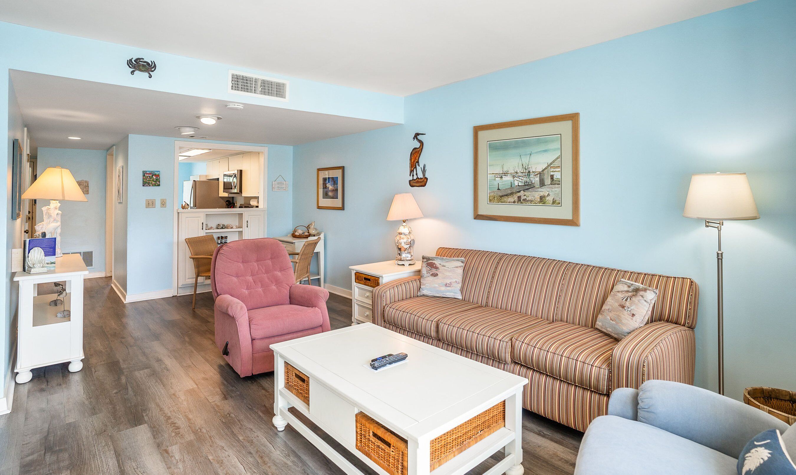 A living room with a pink armchair, a striped sofa, a white coffee table, and a blue armchair.