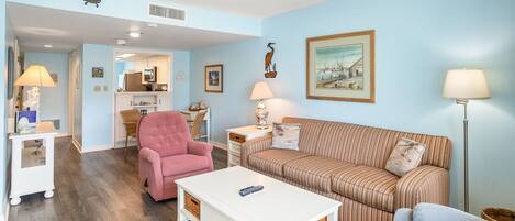 A living room with a pink armchair, a striped sofa, a white coffee table, and a blue armchair.