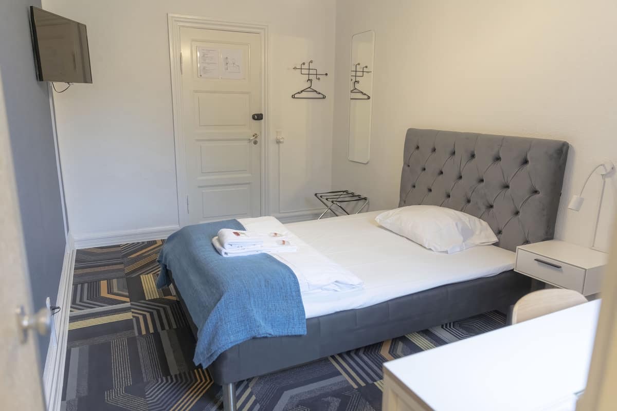 Habitación de hotel con cama, mesita de noche, una silla, televisor montado en la pared y una puerta con un aviso.