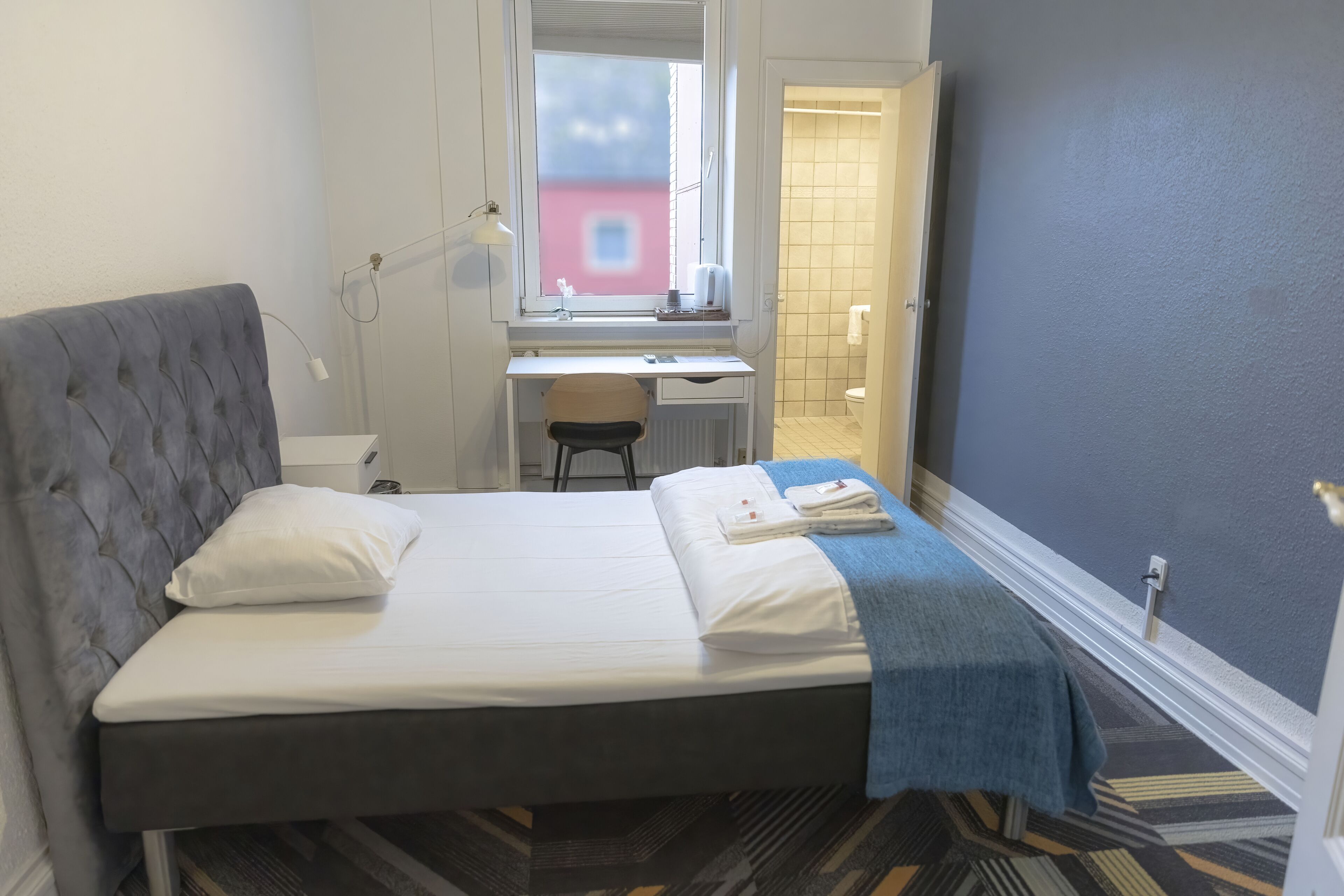 A hotel room with a bed, a desk, a chair, and a window.