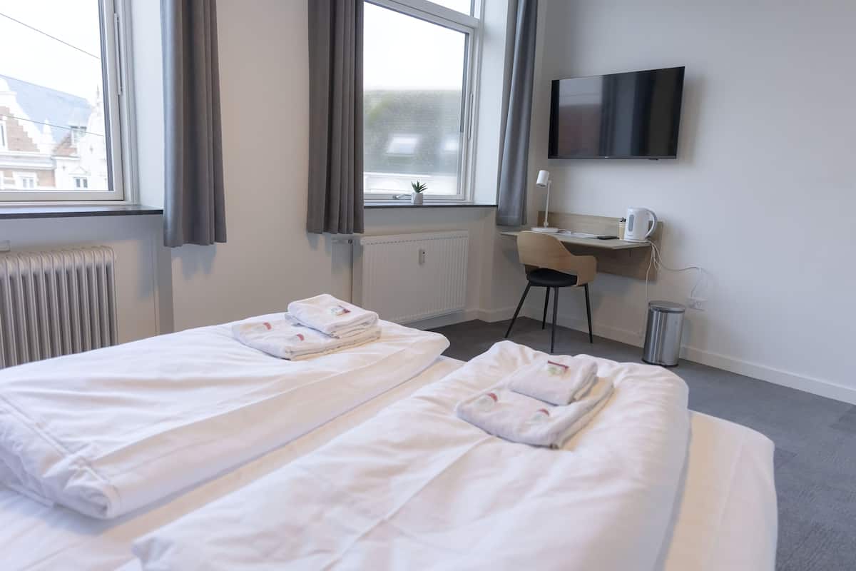 Habitación de hotel con dos camas, un escritorio, una silla, un televisor y un radiador.