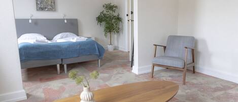 A bedroom with a bed, a chair, a small table, and a potted plant.