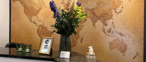 A reception desk with a world map backdrop, a vase with flowers, a Wi-Fi sign, and a hand sanitizer dispenser.
