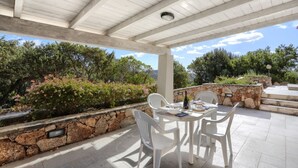 A covered outdoor patio with a stone wall and white plastic chairs.