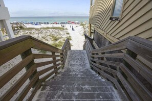 A wooden staircase leading to a beach with umbrellas and people.