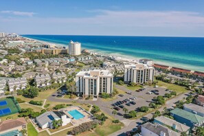 A coastal residential area with a large building complex, a beach, and a parking lot.