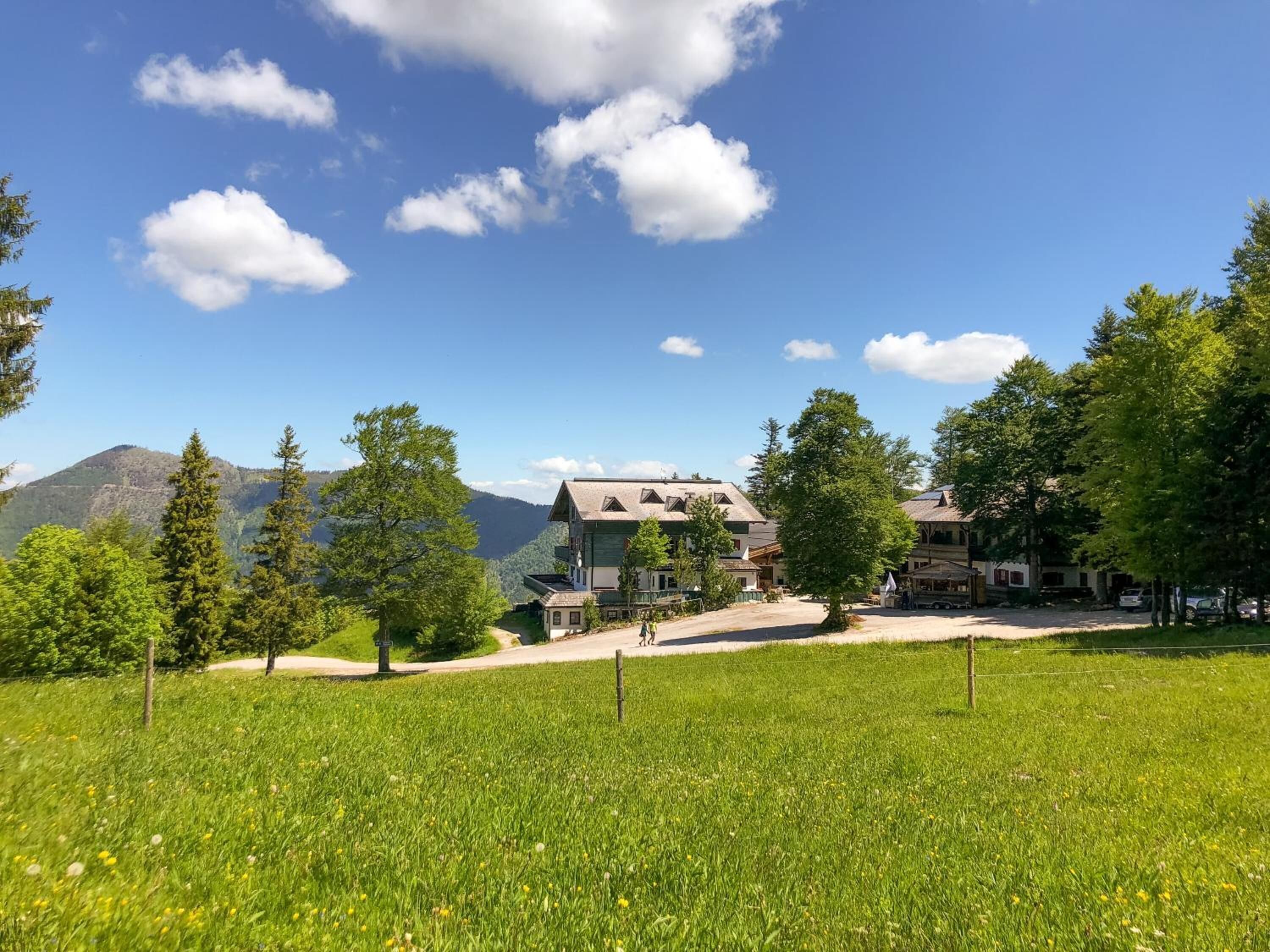 Un hotel con el telón de fondo de una montaña, rodeado de abundante vegetación y un cielo despejado.