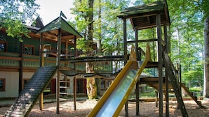 Un parque infantil con tobogán y estructuras para escalar, rodeado de árboles.