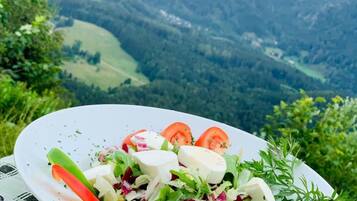 Un piatto di insalata con diverse verdure e formaggio, sullo sfondo di un paesaggio montano.