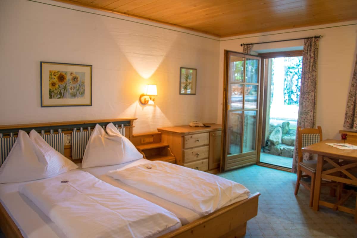 Une chambre avec un lit, un bureau, une chaise et une vue sur l’extérieur, visible à travers une porte vitrée.