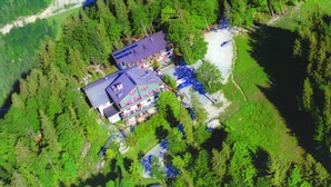 Vista aérea de una cabaña rodeada de bosque denso, con un edificio principal que cuenta con varias terrazas y un estacionamiento.