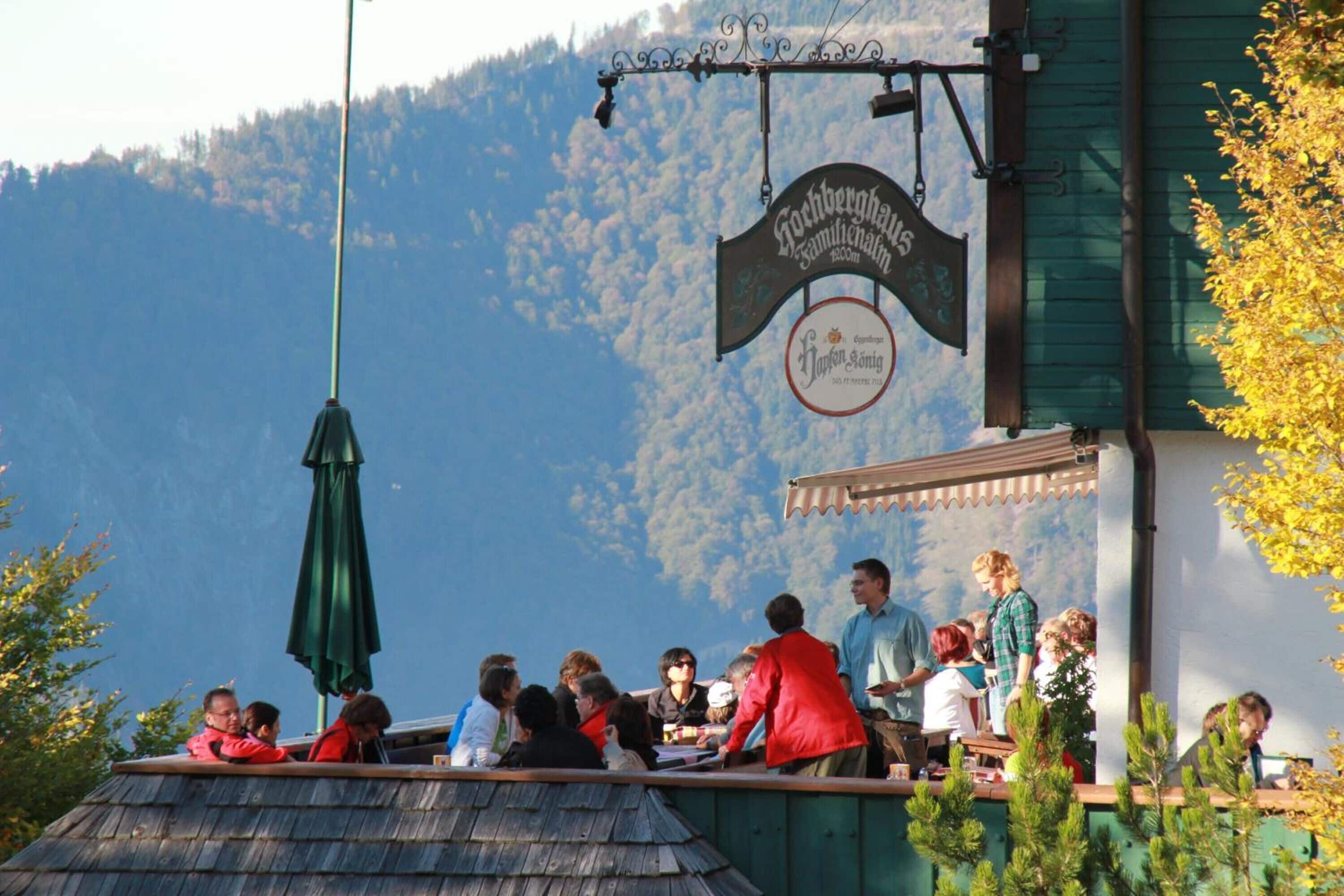 Un grupo de personas cenando en un restaurante al aire libre con montañas de fondo.