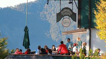Un grupo de personas cenando en un restaurante al aire libre con montañas de fondo.