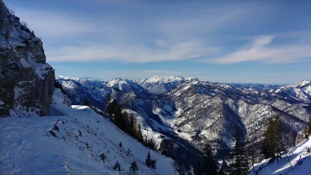 Eine verschneite Berglandschaft mit felsigen Klippen und vereinzelten Bäumen.