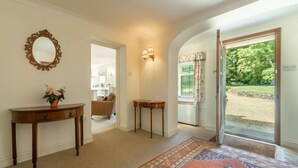 A hallway with a carpeted floor, a wooden console table with a vase, a mirror, and a wall-mounted light fixture. - Beacon Lodge, Burnham Market, Norfolk (Burnham Market)