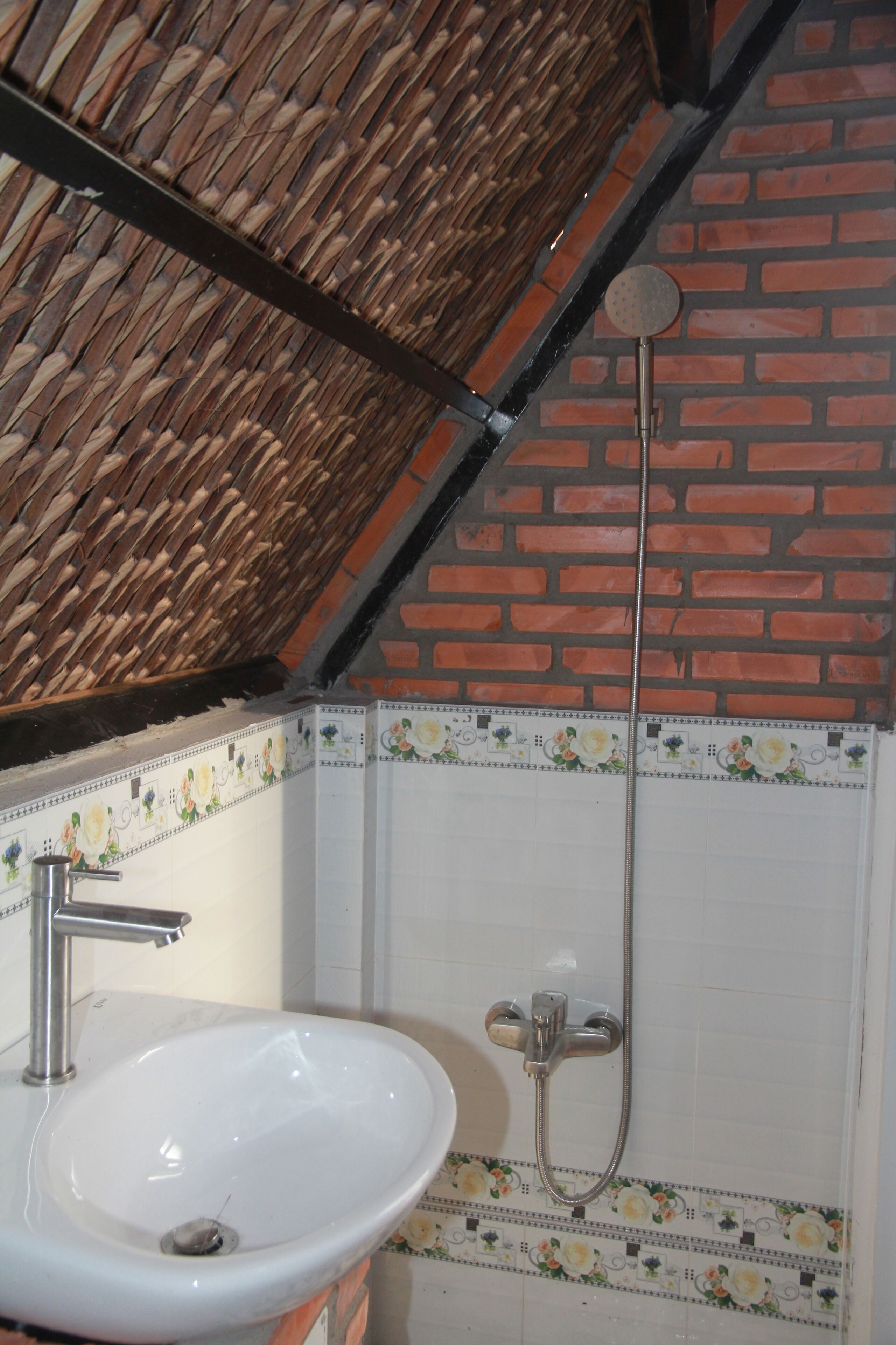 A bathroom with a white sink, a shower, and a tiled wall with floral patterns.