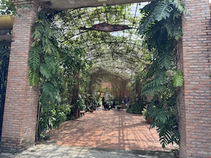 A brick archway leading into a covered garden area with potted plants and a bench. - Bau Bi Mini Farmstay Mekong - Tien Giang (Trung An)
