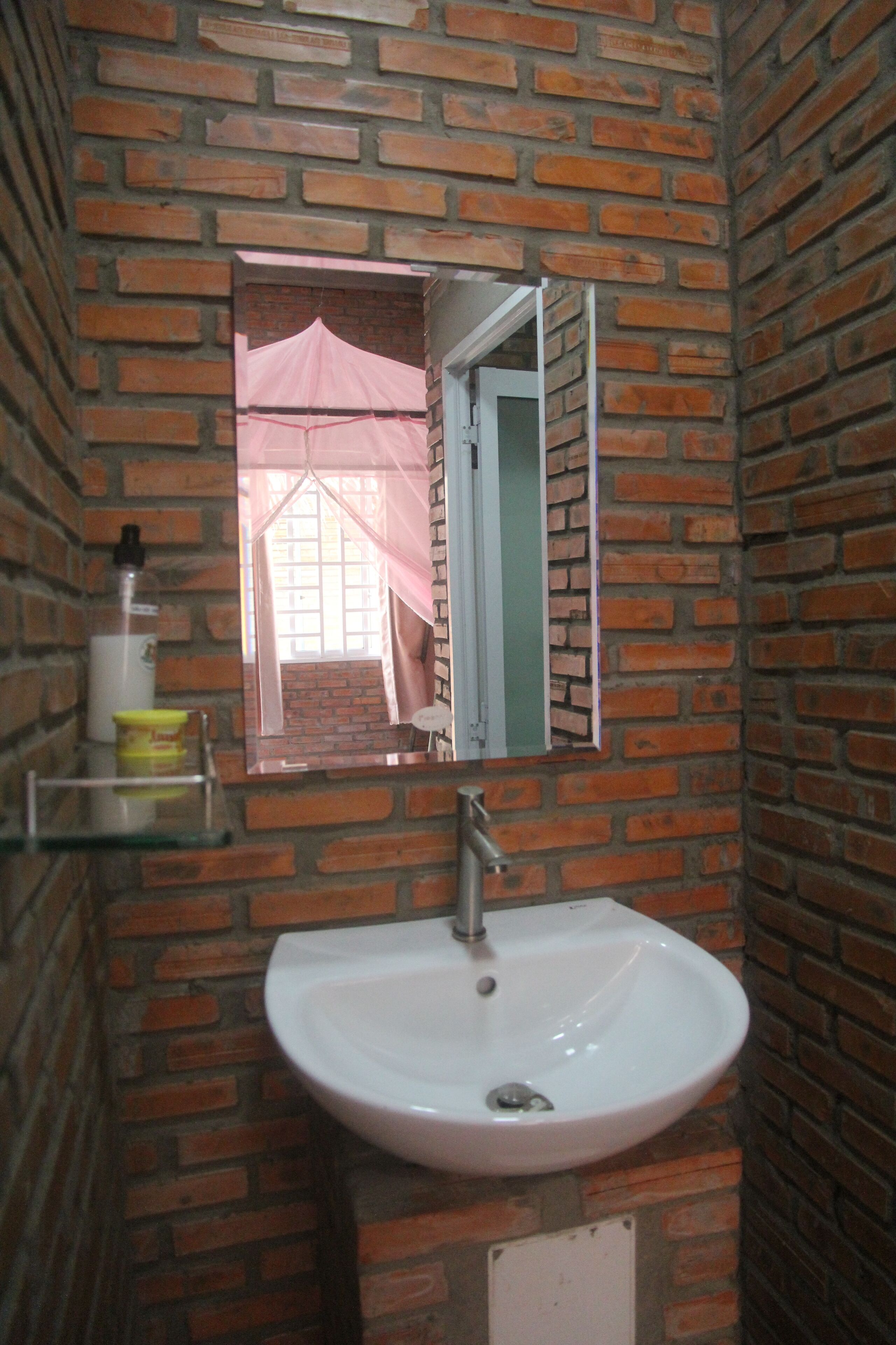 Un baño con un lavabo blanco, un espejo y una pared de ladrillo.
