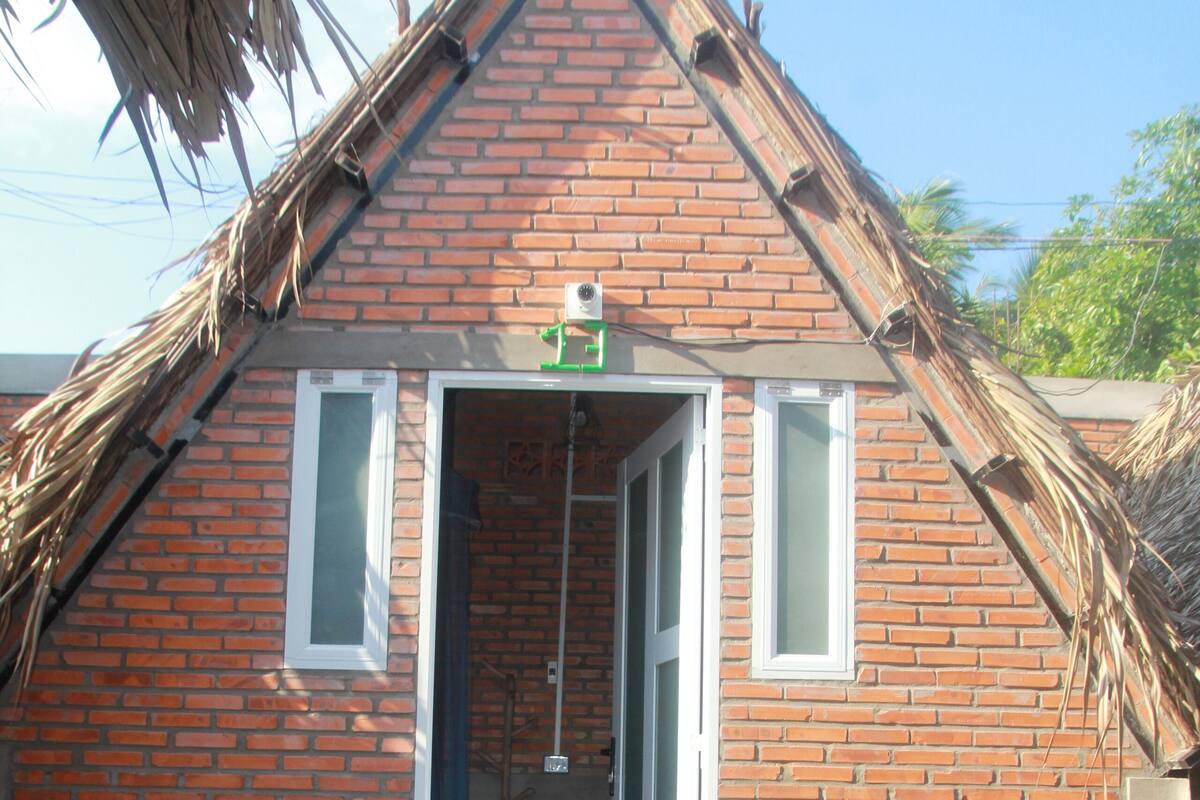 A small brick building with a sloped roof, a door, and a small porch area with a potted plant.