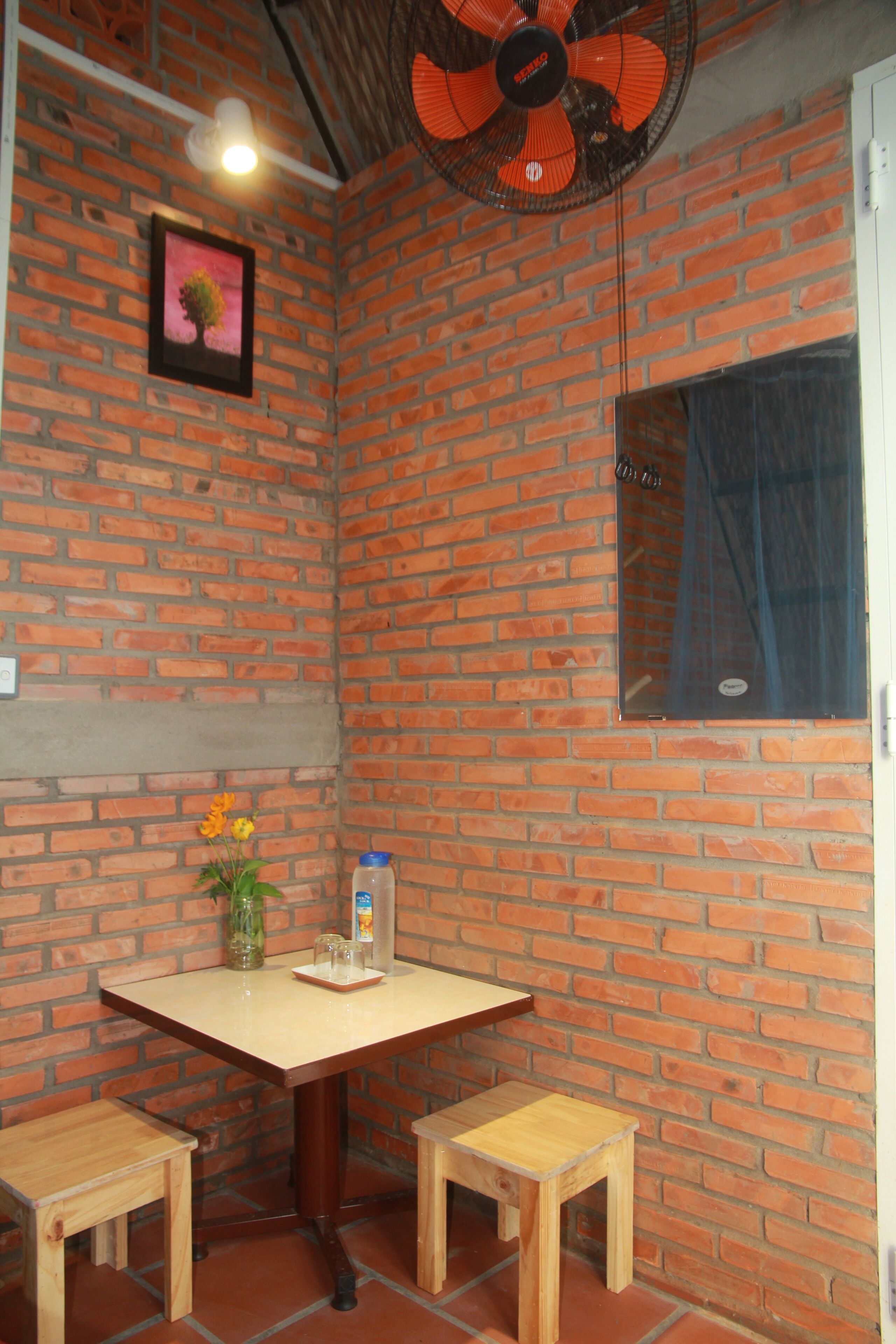 Een kamer met een bakstenen muur, een tafel met twee stoelen, een ventilator en een raam.