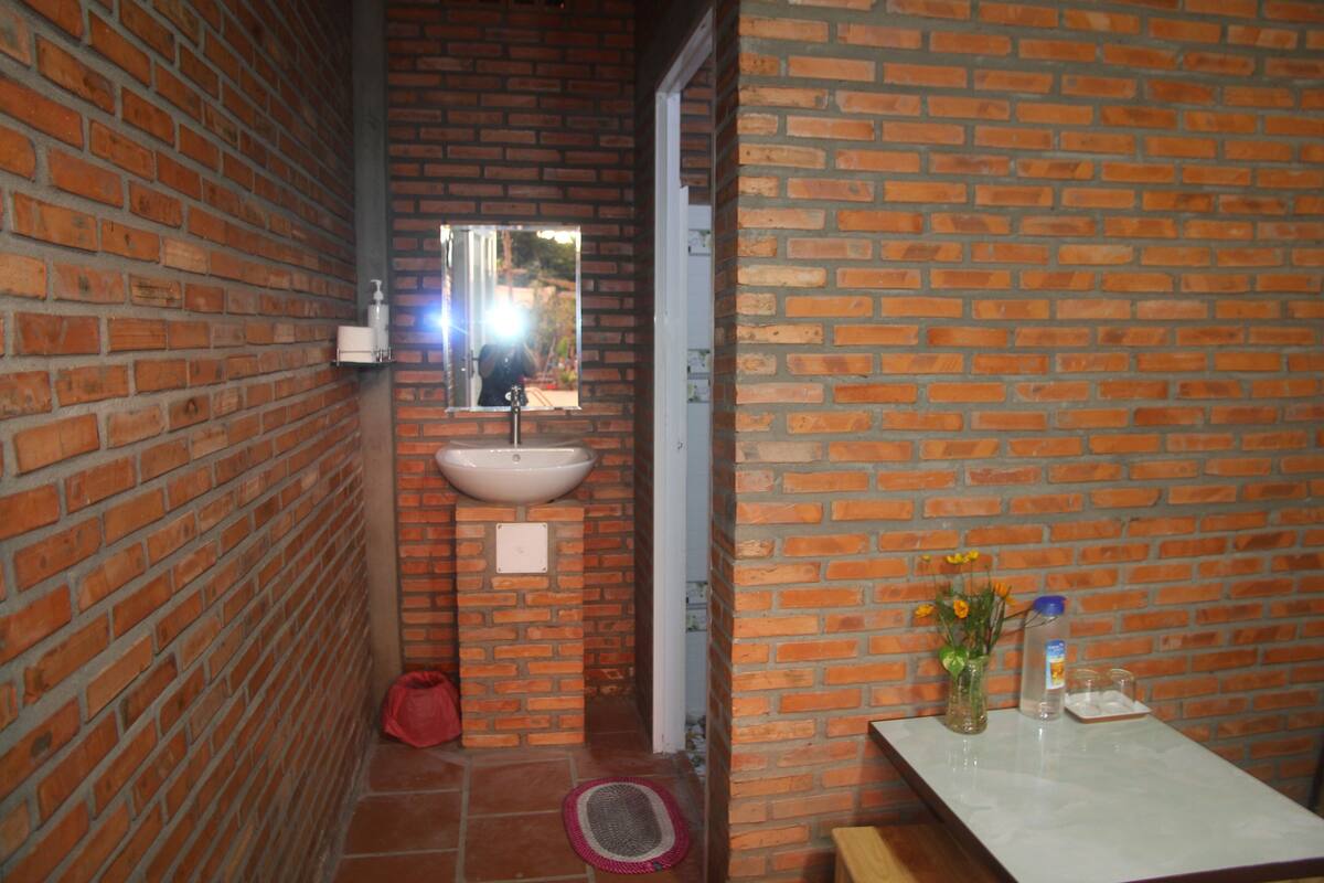 A bathroom with a brick wall, a sink, a mirror, and a small table with toiletries.