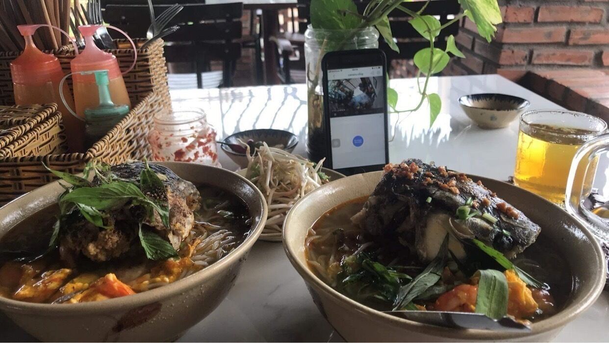 Two bowls of soup with meatballs and vegetables, a smartphone on the table, and a glass of beer.