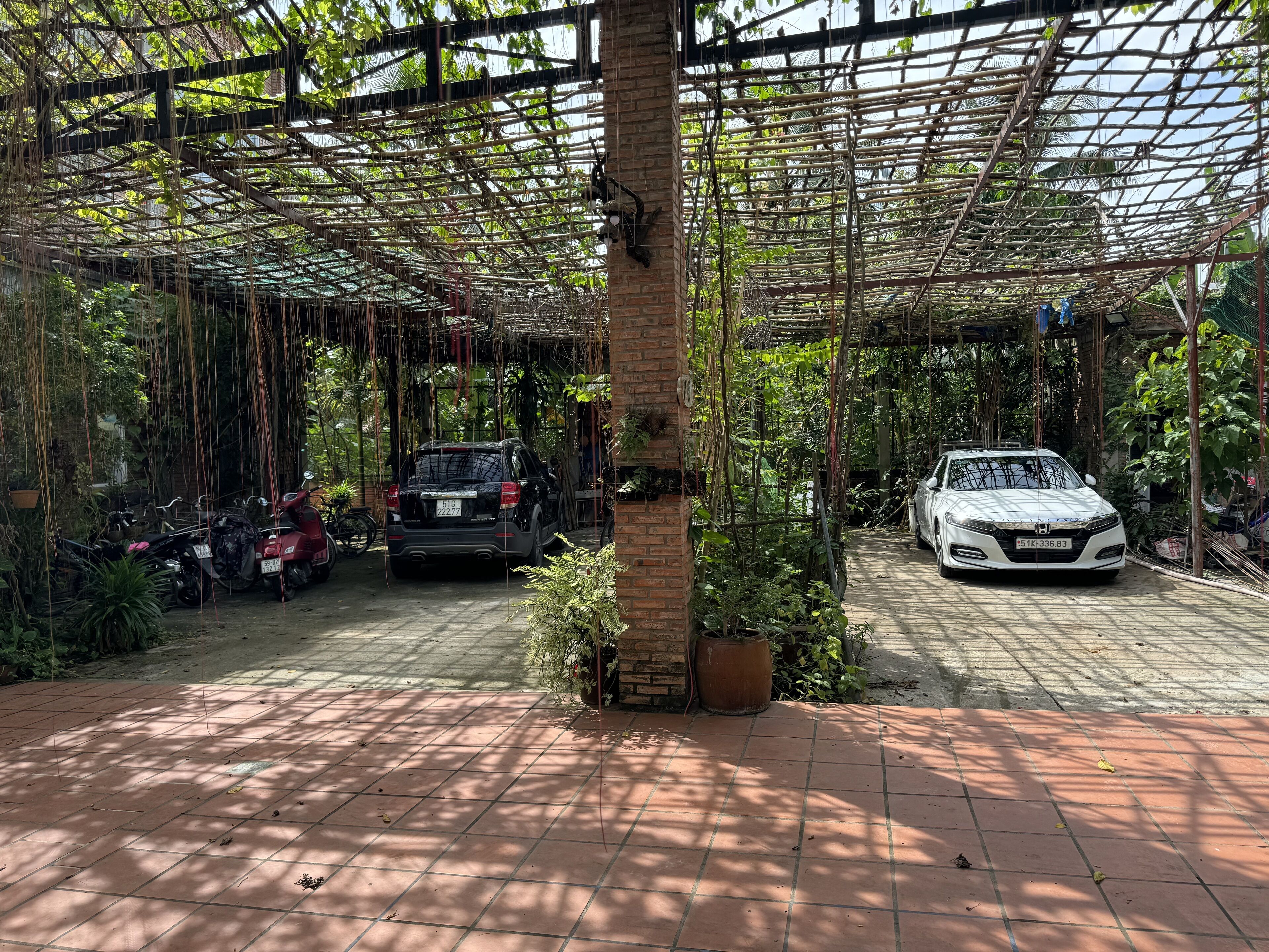 A covered parking area with two cars, a brick wall, and a pergola structure.