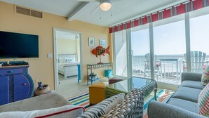 A living room with a television, a sofa, a coffee table, and a balcony with a view of the sea.